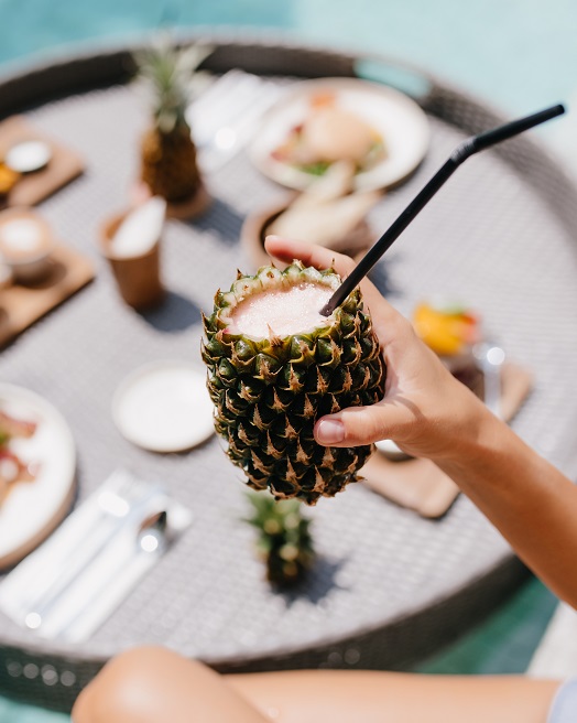 Tanned woman holding sweet pineapple cocktail. Female model posing during lunch in pool.